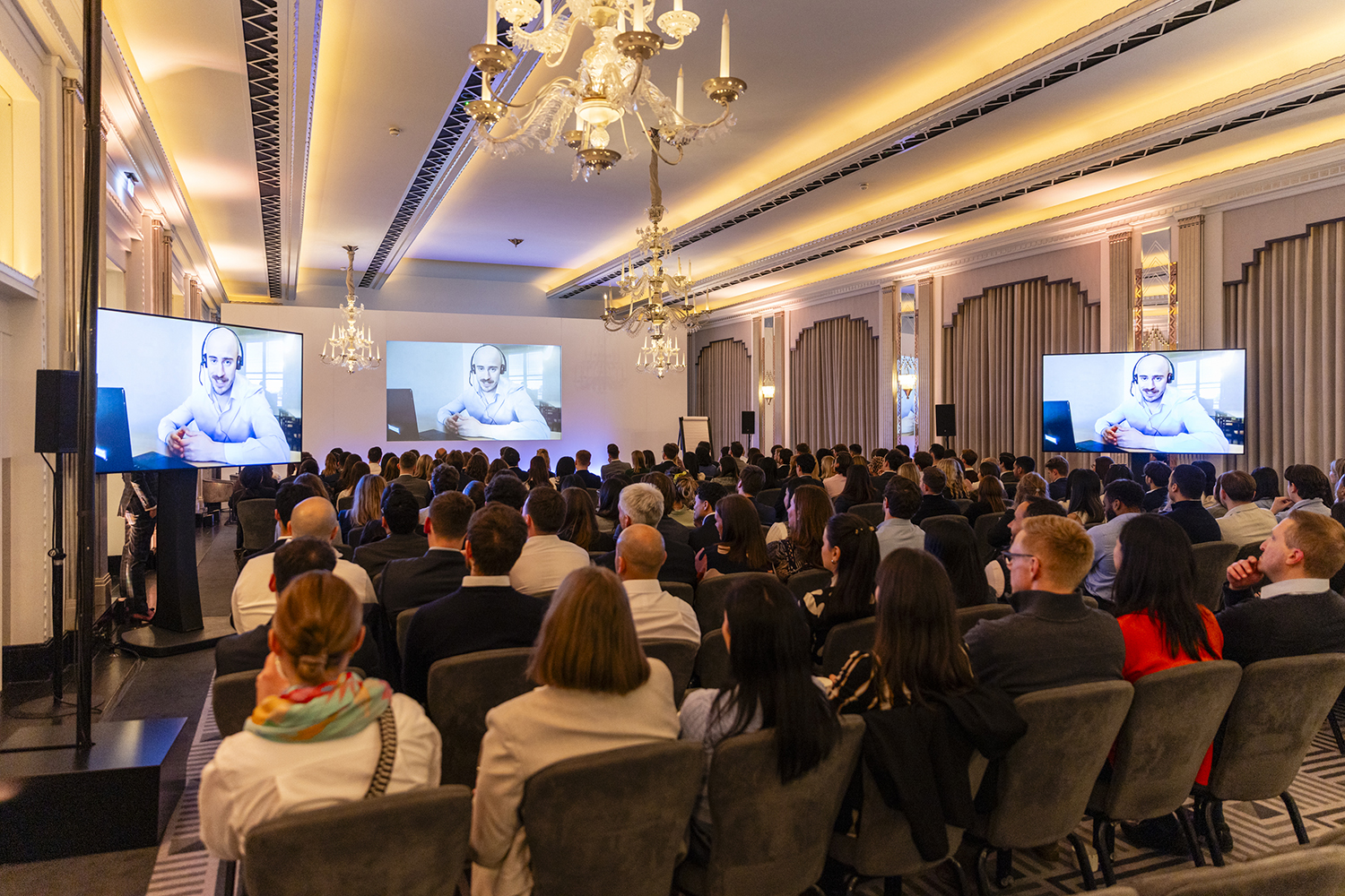 Wide view of conference audience and presentation screens at Claridge’s London event