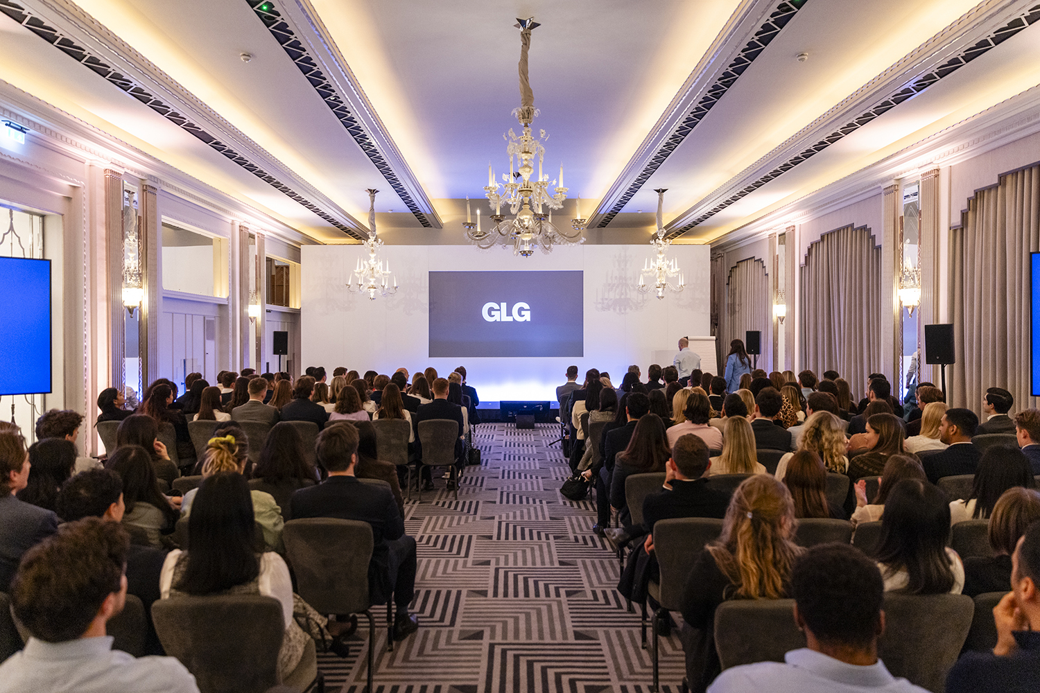 Wide view of conference audience and presentation screens at Claridge’s London event